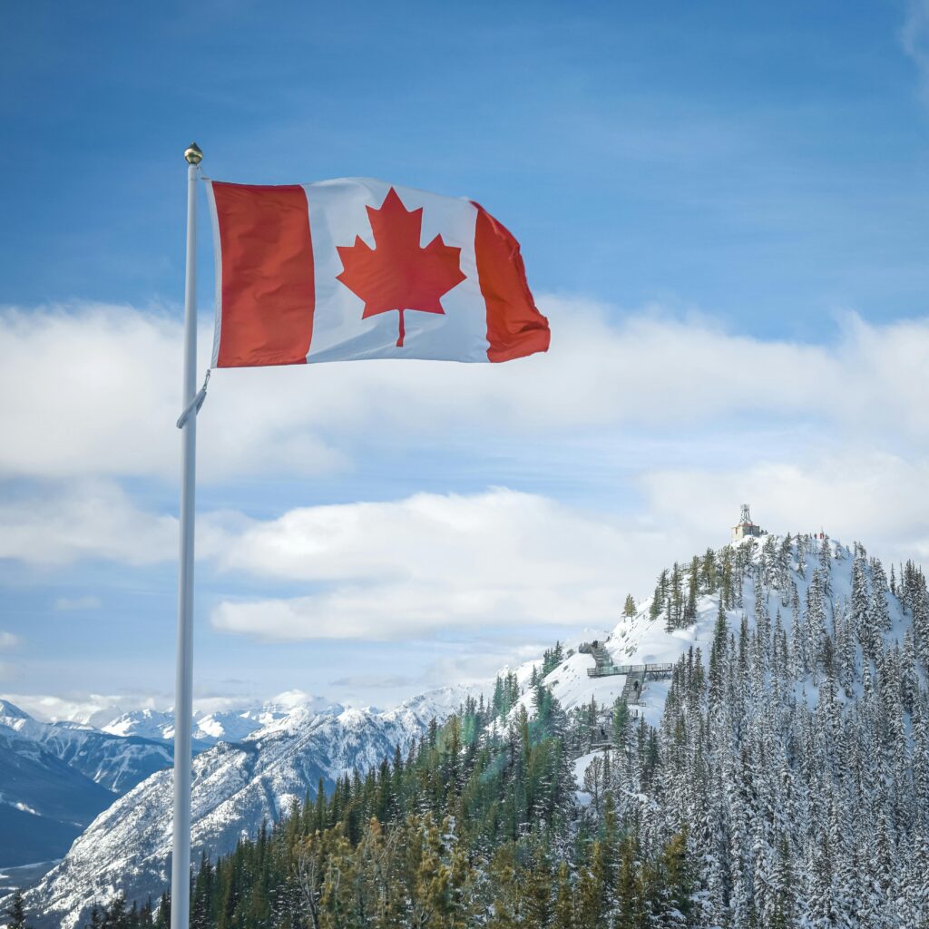 Canadian flag waves proudly against a backdrop of snow-covered mountains in Alberta.